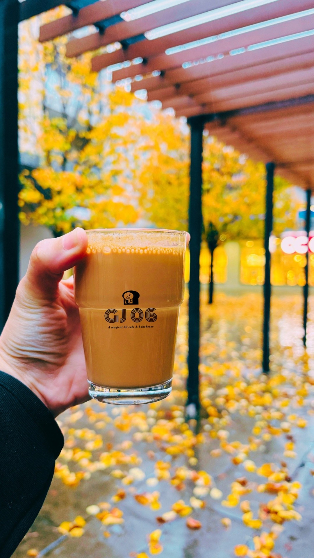 A cutting glass of GJ 06 chai held up among golden autumn leaves